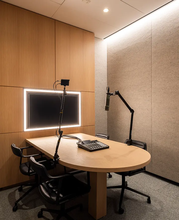 Podcast studio with boom mics, mixer, and led-lit screen in a wood-paneled, sound-treated room.