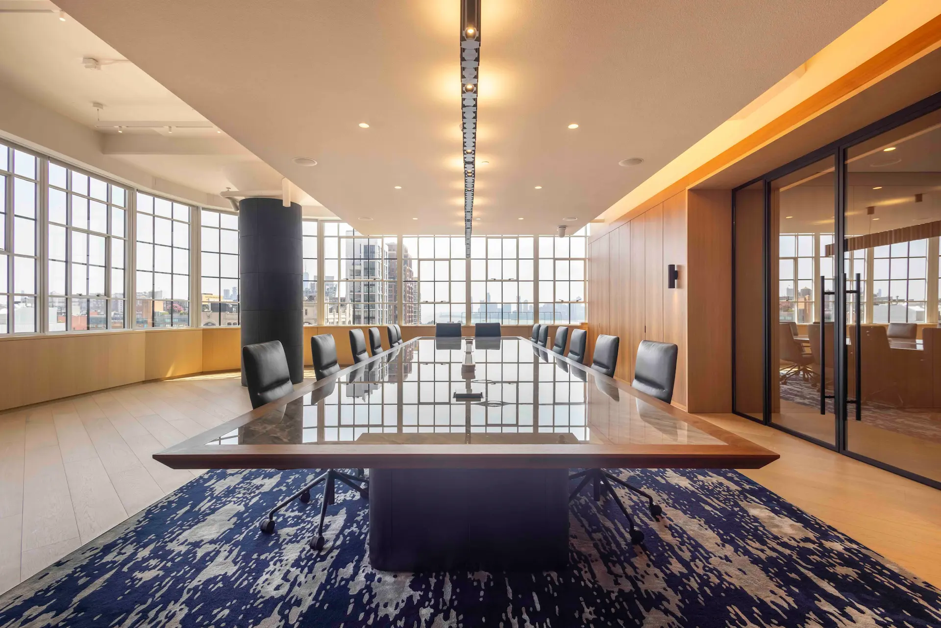Modern meeting room with polished wood table, black leather chairs & panoramic city views through floor-to-ceiling windows.