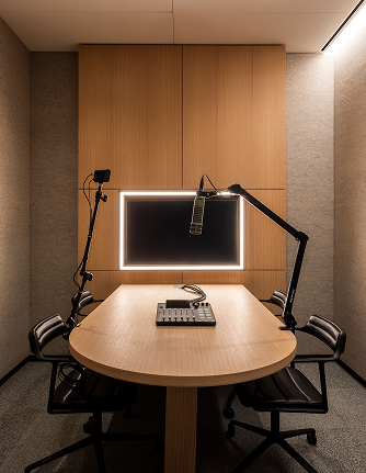 Podcast studio with oval table, boom mics, mixer, and led-framed screen in an acoustically treated space.