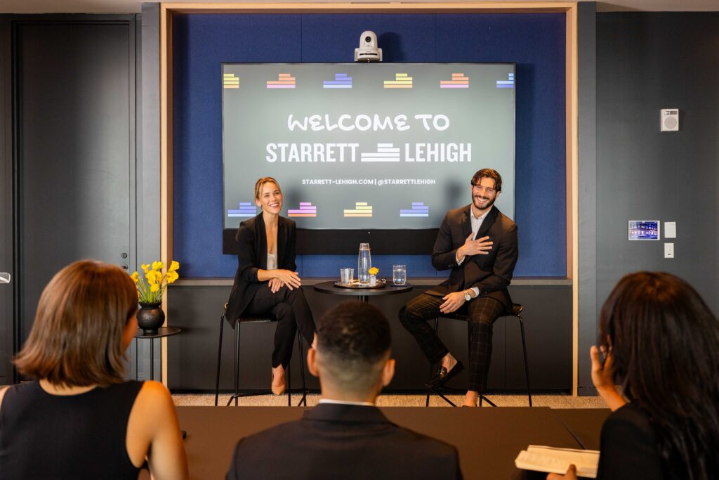 Panel discussion in a modern conference room with speakers seated in front of a screen reading “welcome to starrett lehigh”.