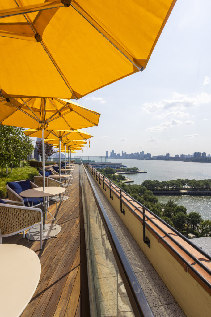 Sunny rooftop terrace with yellow umbrellas, waterfront views, and city skyline in the distance, perfect for outdoor dining.