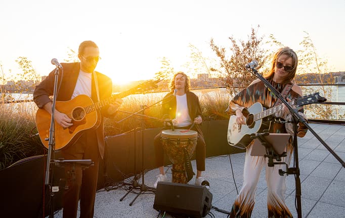 Acoustic band performing outdoors at sunset with guitars and percussion in a warm, intimate setting