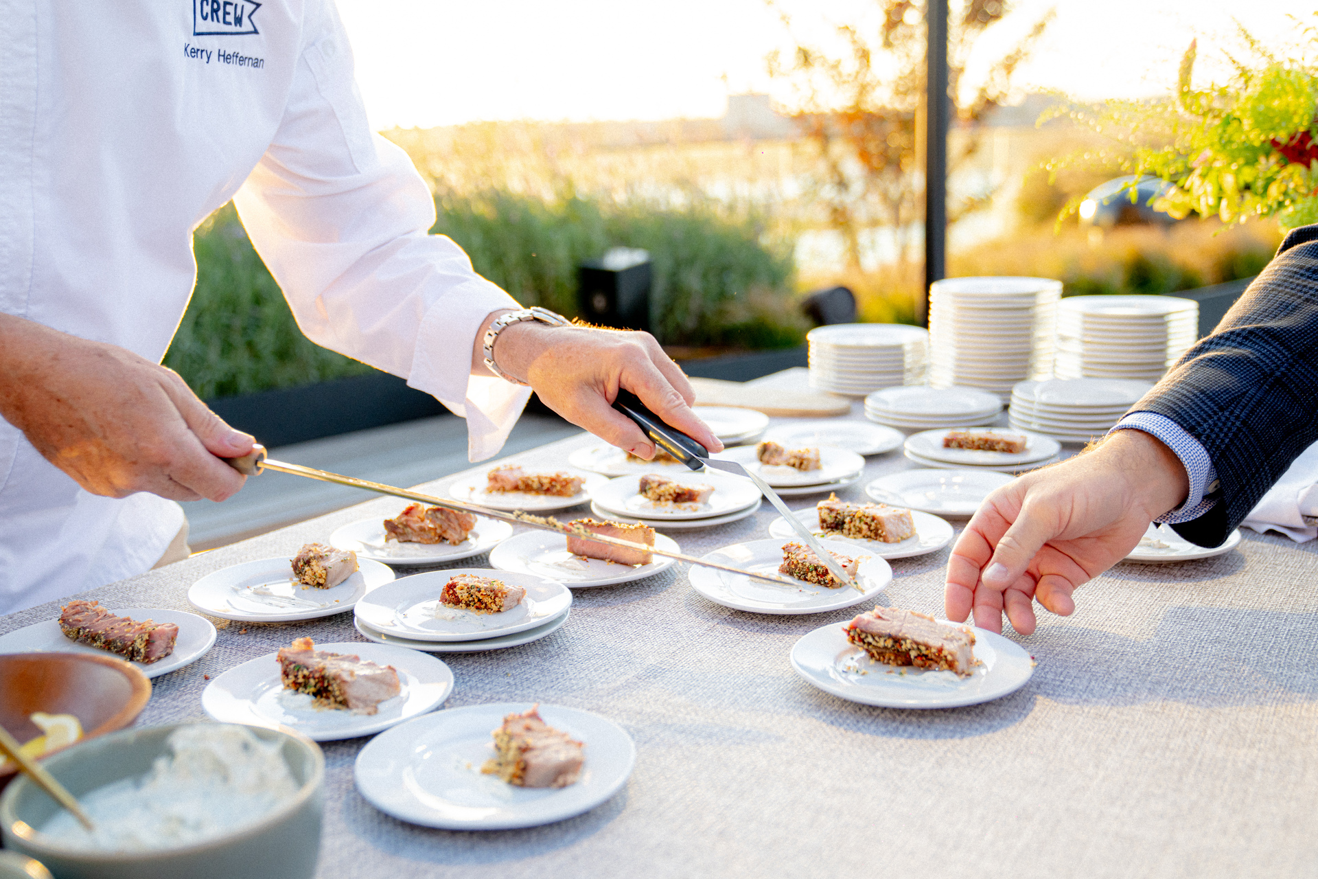 Chef plating seared tuna crusted with spices onto individual appetizer plates during an outdoor waterfront reception