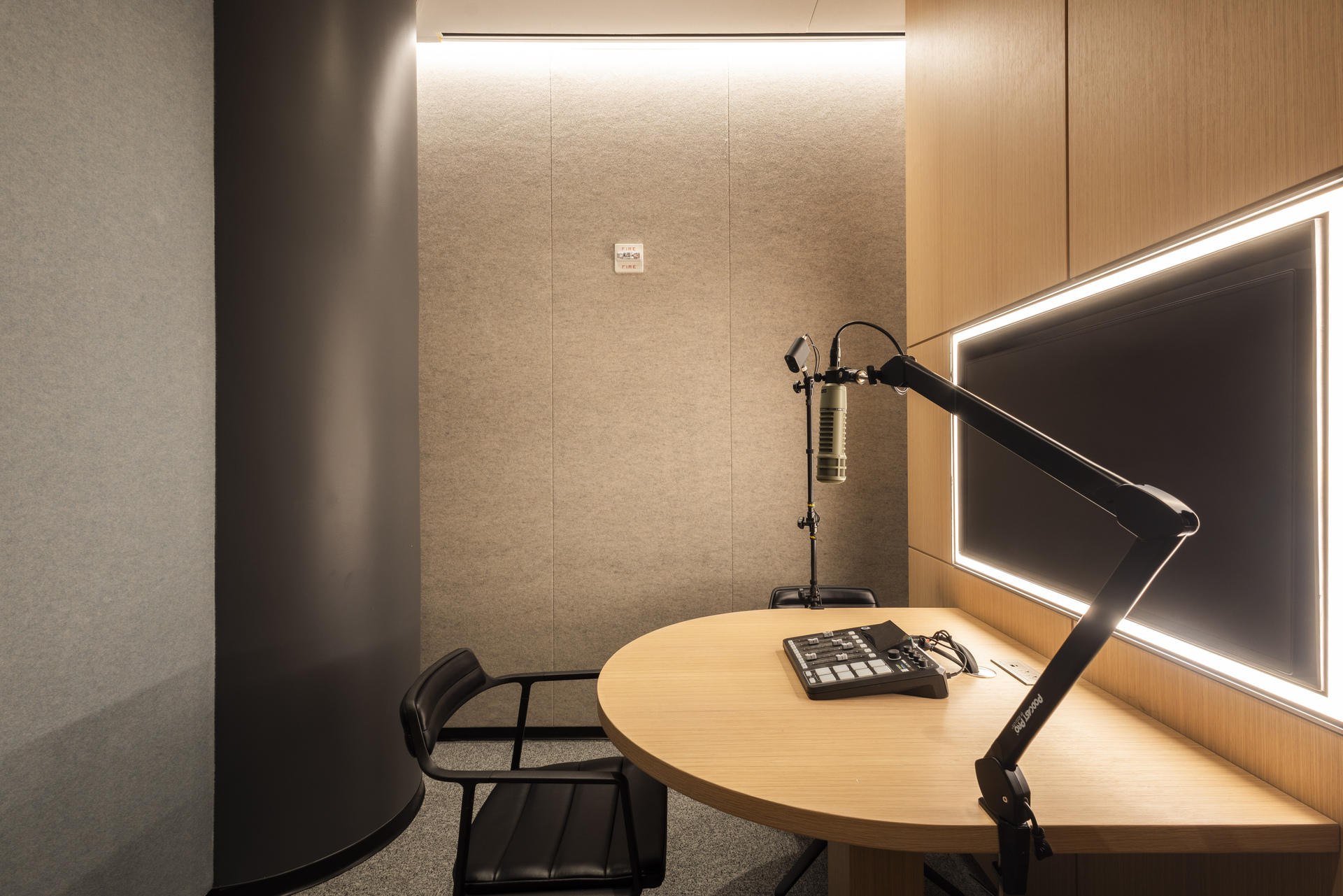 Private podcast and recording studio with acoustic wall treatments, professional broadcast microphone, adjustable boom arm, recording console, and integrated display, designed for content creation and virtual meetings.