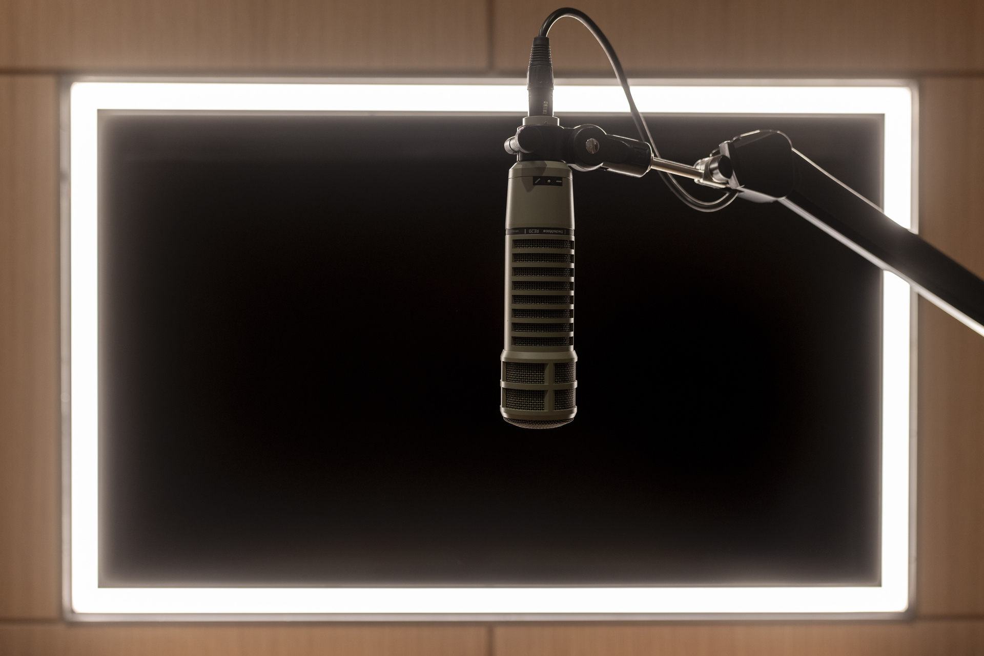 Close-up of a professional broadcast microphone suspended on an adjustable boom arm in a modern podcast studio, framed by illuminated display panels and acoustic finishes for high-quality audio recording.