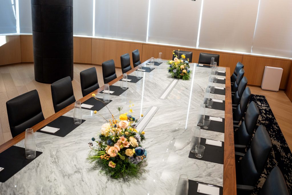 Spacious level10 waterfront event space with professionals networking, large arched industrial windows with river views, open hardwood floor, and curved lounge seating on a navy blue patterned rug